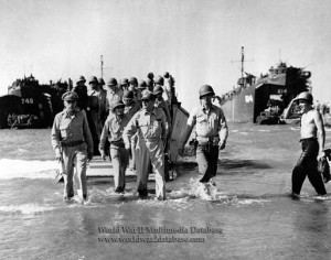 US Army General Douglas MacArthur restages his landing from an LVCP on Leyte, Philippine Islands, for the press on White Beach in the 1st Calvary Division sector. At left is Lieutenant General Richard K. Sutherland, MacArthur's chief of staff, and directly behind MacArthur, in glasses, is Colonel Lloyd Lehrbas, the general's aide. LST-740 and LST-814 are behind him. He originally landed on October 20, 1944, under marginal enemy fire on Red Beach in the 24th Infantry Division sector. Both the Japanese and the Americans were shocked to see him wade ashore on A-Day, the first day of the invasion. The Japanese taunted him verbally and opened fire with a Nambu machine gun, but he was not hurt and reportedly did not duck. Philippine President in exile, Sergio Osmena, accompanied the first landing. The Higgins Boat (LCVP) ran aground, and the party had to walk to shore. MacArthur was upset that his carefully prepared uniform was wet, but the shot was iconic. This view, taken the next day for newsreel cameras, was made on a shallower beach, with less tide. 1st Calvary Division soldiers who saw the photo of the first landing questioned its authenticity, and the controversy over the staged landings began.